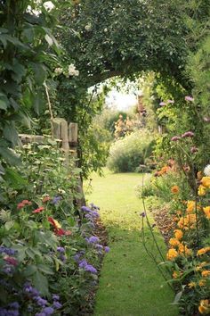 a garden with lots of flowers and plants growing on either side of the path that leads to an open gate