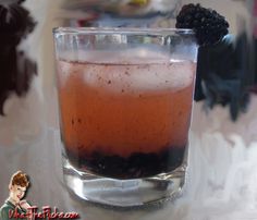 a close up of a drink in a glass with blackberries on the rims