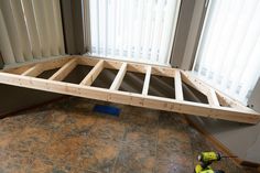 a wooden bed frame laying on top of a hard wood floor next to a window