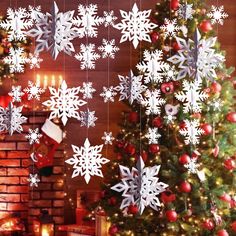 a christmas tree with white snowflakes hanging from it's sides next to a fireplace