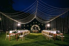 an outdoor wedding reception setup with string lights and tables set up in the grass at night