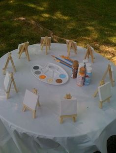 an easel, paintbrushes and other art supplies on a white table cloth