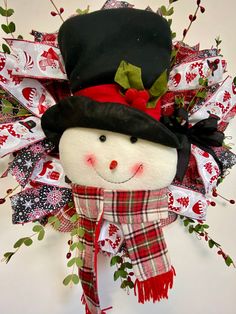 a stuffed snowman wearing a black hat and red scarf with green leaves on it