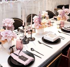 the table is set with black and white plates, silverware, pink flowers and candles