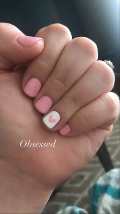 a woman's hand with pink and white nail polish holding up her heart shaped manicure