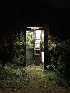 an old phone booth sitting in the middle of a forest at night with its door open