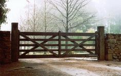 a gate that is next to a stone wall and trees in the background on a foggy day