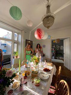 two women standing at a table with food on it and paper lanterns hanging from the ceiling