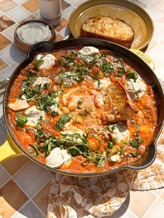 a skillet filled with meat and vegetables on top of a table next to bread