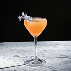 a glass filled with a drink sitting on top of a marble counter next to a flower