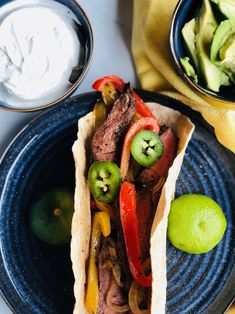 two tacos on a plate next to a bowl of sour cream and limes