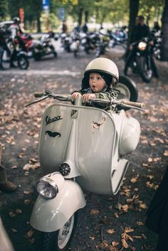 a little boy riding on the back of a white scooter with a helmet