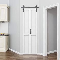 an empty room with white walls and wooden floors, two doors open to reveal the kitchen