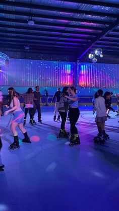 group of people skating on an indoor ice rink at night with colorful lights in the background