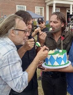 three men standing in front of a cake with green icing and one man holding a knife