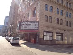 an old movie theater with cars parked on the side of the street in front of it