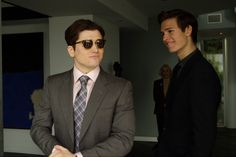 two men in suits and sunglasses standing next to each other with one man looking at the camera