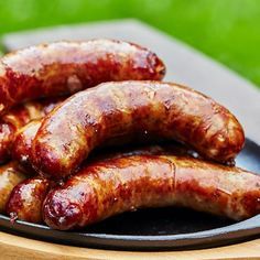 three sausages on a black plate sitting on top of a wooden table next to a green lawn