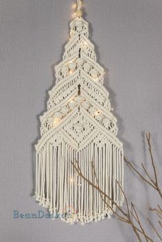 a crocheted christmas tree hanging on a wall next to some branches with lights