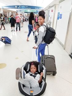 a woman pushing a baby in a stroller at an airport with other people walking by