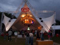 a group of people standing in front of a white tent with red hearts on it