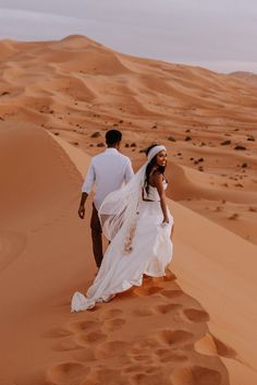 a bride and groom walking through the sand dunes at their desert wedding in morocco, africa