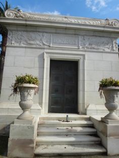 two large white urns sitting in front of a building with plants growing out of it