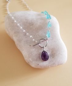 Three amazing crystals joined together into one fabulous necklace!On one side of necklace is a row of raw natural Apatite nuggets that are hand wire wrapped and joined to a dainty Moonstone beaded chain. A natural Amethyst teardrop hangs from the modern toggle clasp that completes this beautiful unique necklace.Details:* Raw natural Apatite nuggets Size about 12 mm* Natural beaded Moonstone Chain* Natural Bezel Set Amethyst Teardrop Size about 14 mm* Sterling Silver Wire* Toggle is Silver-Rhodiu Adjustable Amethyst Gemstone Bead Crystal Necklace, Handmade Blue Amethyst Necklace, Handmade Blue Amethyst Crystal Necklaces, Handmade Blue Amethyst Crystal Necklace, Handmade Elegant Apatite Necklace, Purple Raw Stone Crystal Necklace For Healing, Adjustable Hand-wrapped Amethyst Crystal Necklace, Amethyst Stone Necklace, Spring Jewelry Trends