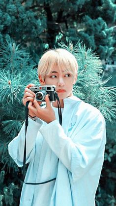 a person taking a photo with a camera in front of some trees and pine needles