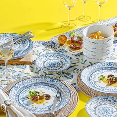 a table topped with blue and white plates covered in food next to glasses of wine