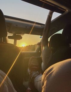 two people sitting in the back seat of a car as the sun sets behind them