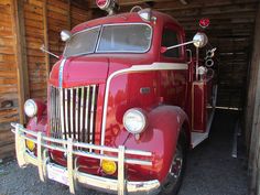 an old red fire truck parked in a garage next to a wall with wood paneling