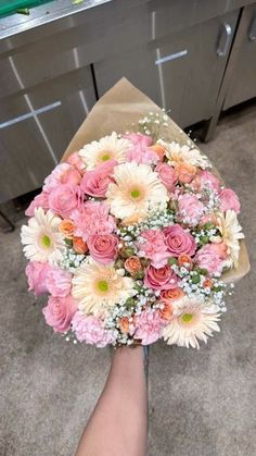 someone holding a bouquet of pink and white flowers in front of a stove top oven