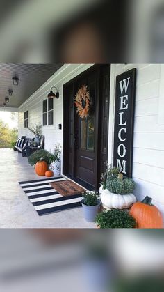 front porch decorated for fall with pumpkins and greenery on the steps, black and white striped rug