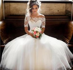 a woman sitting on top of a piano wearing a white dress and holding a bouquet