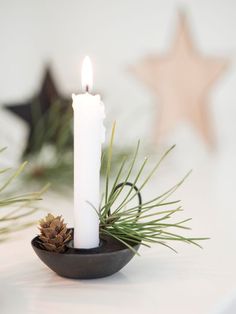 a white candle sitting on top of a bowl filled with pine cones