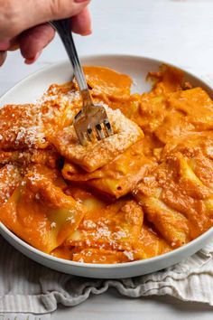 a person holding a fork in a bowl of food with sauce and cheese on top