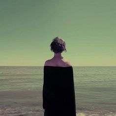 a woman standing on the beach looking out at the ocean with her back to the camera