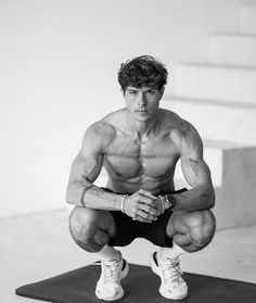 a shirtless man squatting on a mat