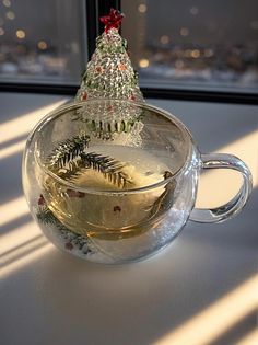 a glass cup filled with tea next to a christmas tree on top of a window sill