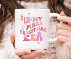 a woman is holding a coffee mug with the words merry pink christmas era on it