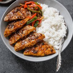 a plate with chicken, rice and vegetables next to a fork on a table top