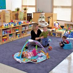 a woman sitting on the floor with two children in a room full of books and toys