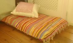 a small bed with a colorful blanket on top of it next to a wooden floor