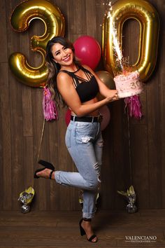 a woman holding a cake and balloons in front of a wooden wall with the number 30 on it