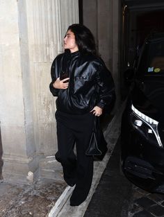 a woman in black jacket and pants standing next to a car