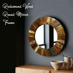 a round mirror sitting on top of a wooden dresser next to a vase and cup