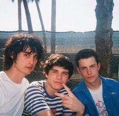 three young men sitting next to each other in front of a fence and palm trees