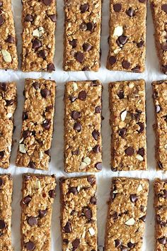 several squares of granola bars lined up on a sheet of parchment paper with chocolate chips and almonds