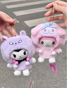 two small stuffed animals hanging from strings on a pole in front of a person's hand